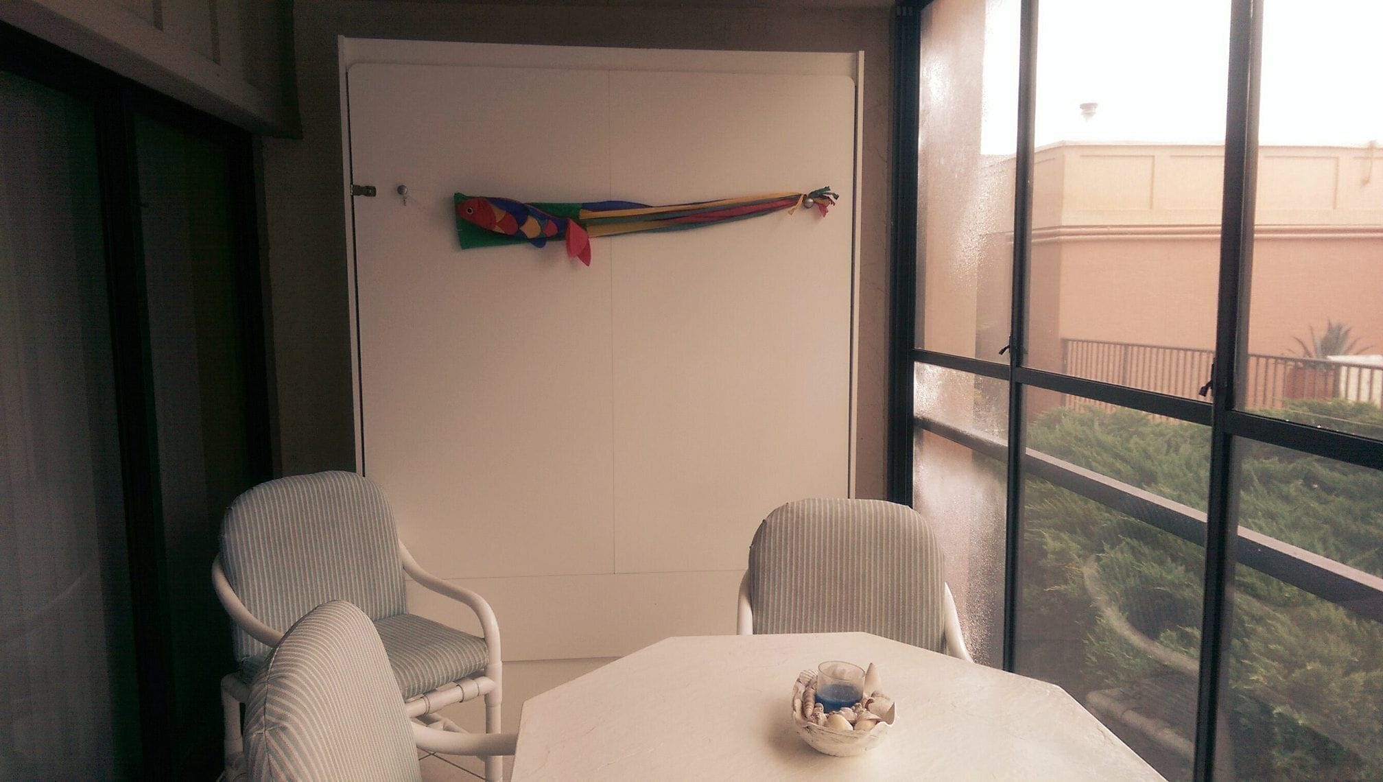 A small balcony with two striped chairs, a white table, and a decorative hanging.