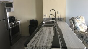 A kitchen with a marble countertop, stainless steel appliances, and a black trash bin. - GOLF  BOATING BIKING (Punta Gorda)