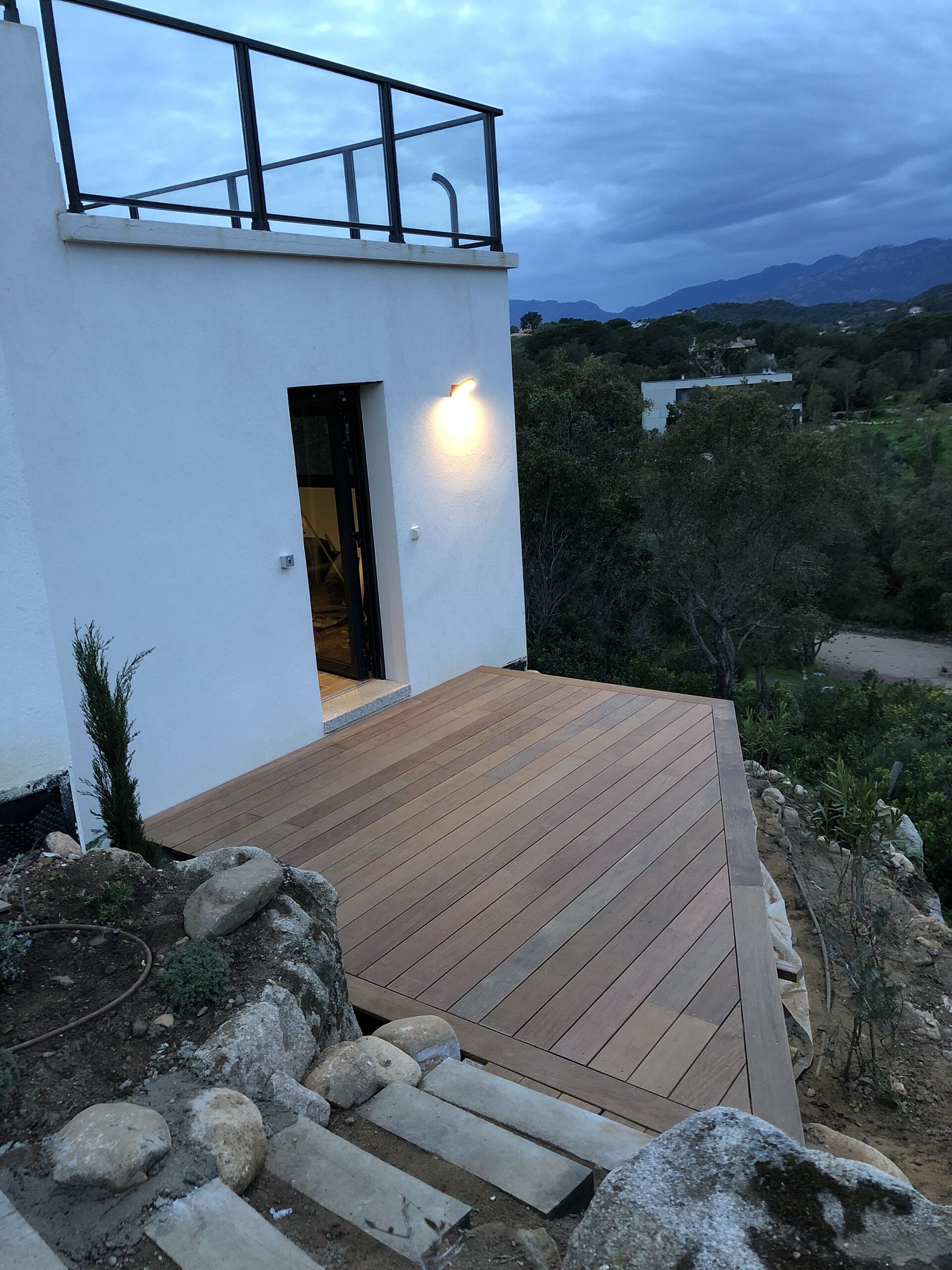 A modern building with a wooden deck, a balcony with a metal railing, and a view of the surrounding landscape.
