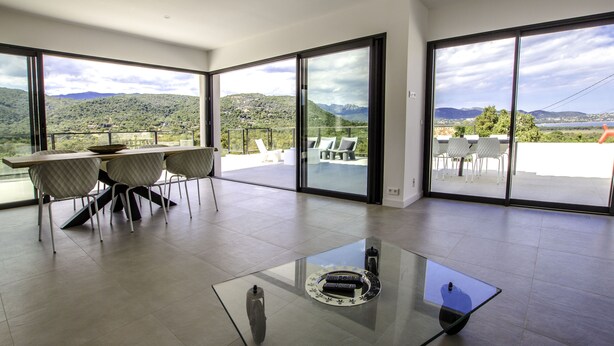 A spacious room with a glass table, a dining area with chairs, and large sliding glass doors offering a mountain view. - MODERN HOUSE PORTO VECCHIO AIR-CONDITIONED PRIVATE POOL SUPERB SEA/MOUNTAIN VIEW (Zonza)