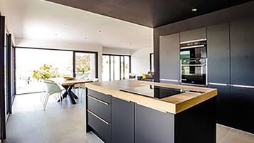 Une cuisine moderne dotée d’un îlot central, de meubles de couleur sombre et offrant une vue sur l’extérieur.