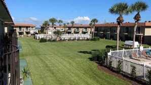 A residential area with multiple two-story buildings, a well-maintained lawn, and a fenced patio area with chairs. - Live the Beach Life! Stay in our FUN & AMAZING Townhome! (St Augustine)