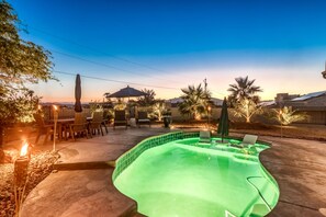 A swimming pool with a green interior, surrounded by patio furniture and palm trees.