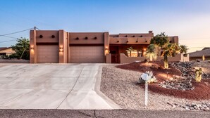 Una casa moderna con dos garajes, un camino de acceso y un jardín ajardinado con cactus y rocas.