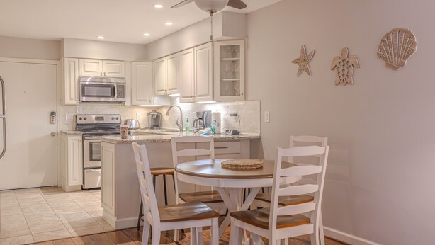 A kitchen with white cabinets, a microwave, stove, and a dining area with a round table and chairs. - First Floor, Updated, and a Short Walk to the Beach (Hilton Head Island)