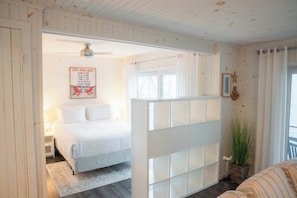 Une chambre à coucher comprenant un lit, une table de chevet, une cloison blanche, un ventilateur de plafond, une fenêtre et un panneau affichant les règles.