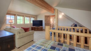 Une chambre mansardée chaleureuse, avec un escalier en bois, une télévision et un canapé confortable.