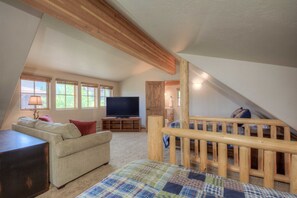 A cozy attic bedroom with a wooden staircase, a television, and a comfortable sofa.
