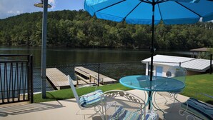 A patio with a table and chairs, a blue umbrella, and a view of a lake and forest. - Stylish Lakefront Home - Last Minute Getaway for the Summer (Hot Springs)