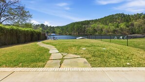 A backyard with a stone pathway, a fenced area, and a view of a lake and forested hill. - Stylish Lakefront Home - Last Minute Getaway for the Summer (Hot Springs)