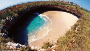 A natural rock formation with a beach and clear blue waters.