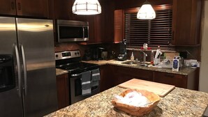 A kitchen with granite countertops, stainless steel appliances, wooden cabinets, and pendant lighting.