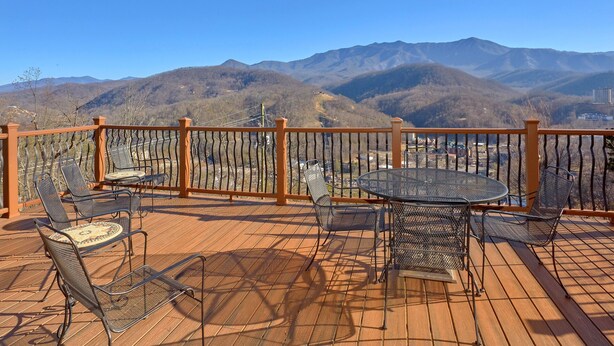 Terraza de madera con sillas metálicas y una mesa, con vista a un paisaje montañoso.