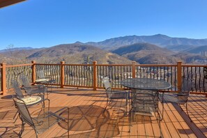 A wooden deck with metal chairs and a table, overlooking a mountainous landscape.