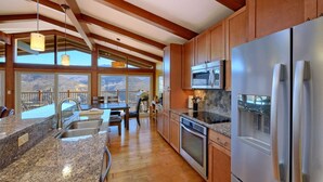 Una cocina con encimeras de granito, electrodomésticos de acero inoxidable, armarios de madera y vistas a montañas a través de amplias ventanas.
