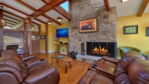 Un salón espacioso con sofás de cuero, una chimenea de piedra y un televisor montado en la pared.