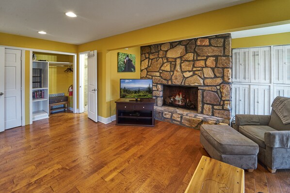 A living room with hardwood flooring, a stone fireplace, a television, and a gray couch.