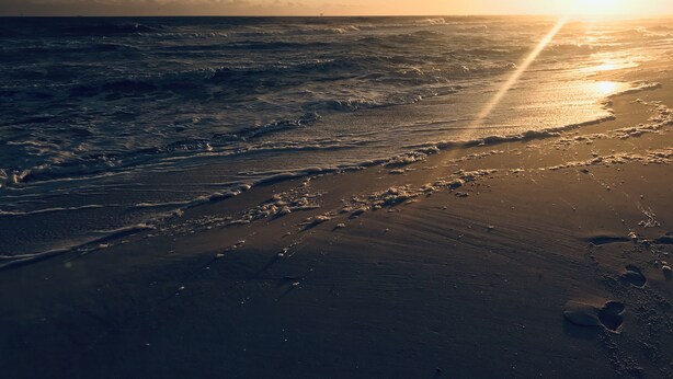 A beach with waves and a sunset.