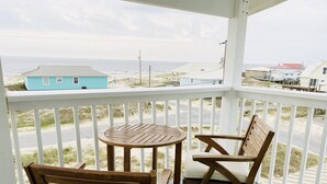 A wooden deck with a table and two chairs, overlooking a beach and ocean.