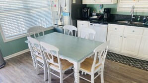 A dining area with a table and chairs, a refrigerator, a coffee maker, and a sink.