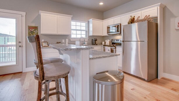 A modern kitchen with white cabinets, a stainless steel refrigerator, a microwave, and a granite countertop. - Razorback Getaway Close to University!  (Fayetteville)