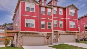 A multi-story residential building with a red exterior, two garage doors, and a brick foundation. - Razorback Getaway Close to University!  (Fayetteville)