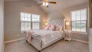A bedroom with a tufted headboard, a bed with patterned bedding, two bedside lamps, and a ceiling fan. - Razorback Getaway Close to University!  (Fayetteville)