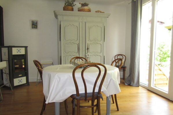 A dining area with a table set for four, surrounded by wooden chairs, a white cabinet with decorative items, and a view of a wooden deck through a window.