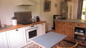 Una cocina compacta con armarios blancos, encimera de madera, una mesa pequeña y un horno empotrado.