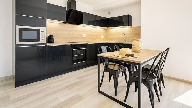Una cocina moderna con armarios negros, encimera de madera y un comedor con mesa y sillas.