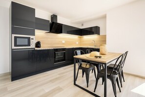 A modern kitchen with black cabinetry, a wooden countertop, and a dining area with a table and chairs. - Cozy Beachside Stay – A/C, Wi-Fi, Comfort & Calm (Canet-en-Roussillon)