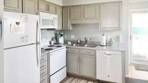 A compact kitchen with white appliances, a built-in microwave, a coffee maker, and a dishwasher. - ☀ Breezy, Open Condo, Steps from Beach and Boardwalk with Ocean Views & Pool ☀  (Carolina Beach)