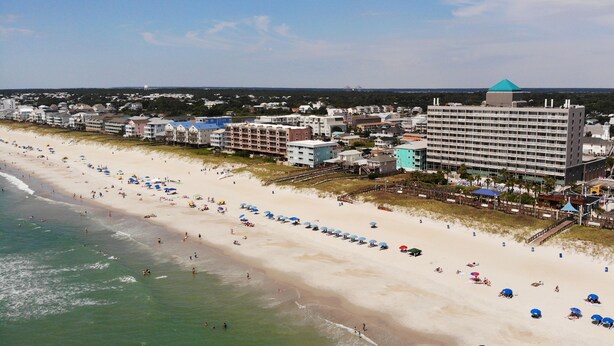 A beach with a row of beach umbrellas and a hotel in the background. - ☀ Breezy, Open Condo, Steps from Beach and Boardwalk with Ocean Views & Pool ☀  (Carolina Beach)