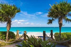 Un sentier en bois mène à une plage où l’eau est d’un bleu turquoise limpide et le ciel est dégagé.
