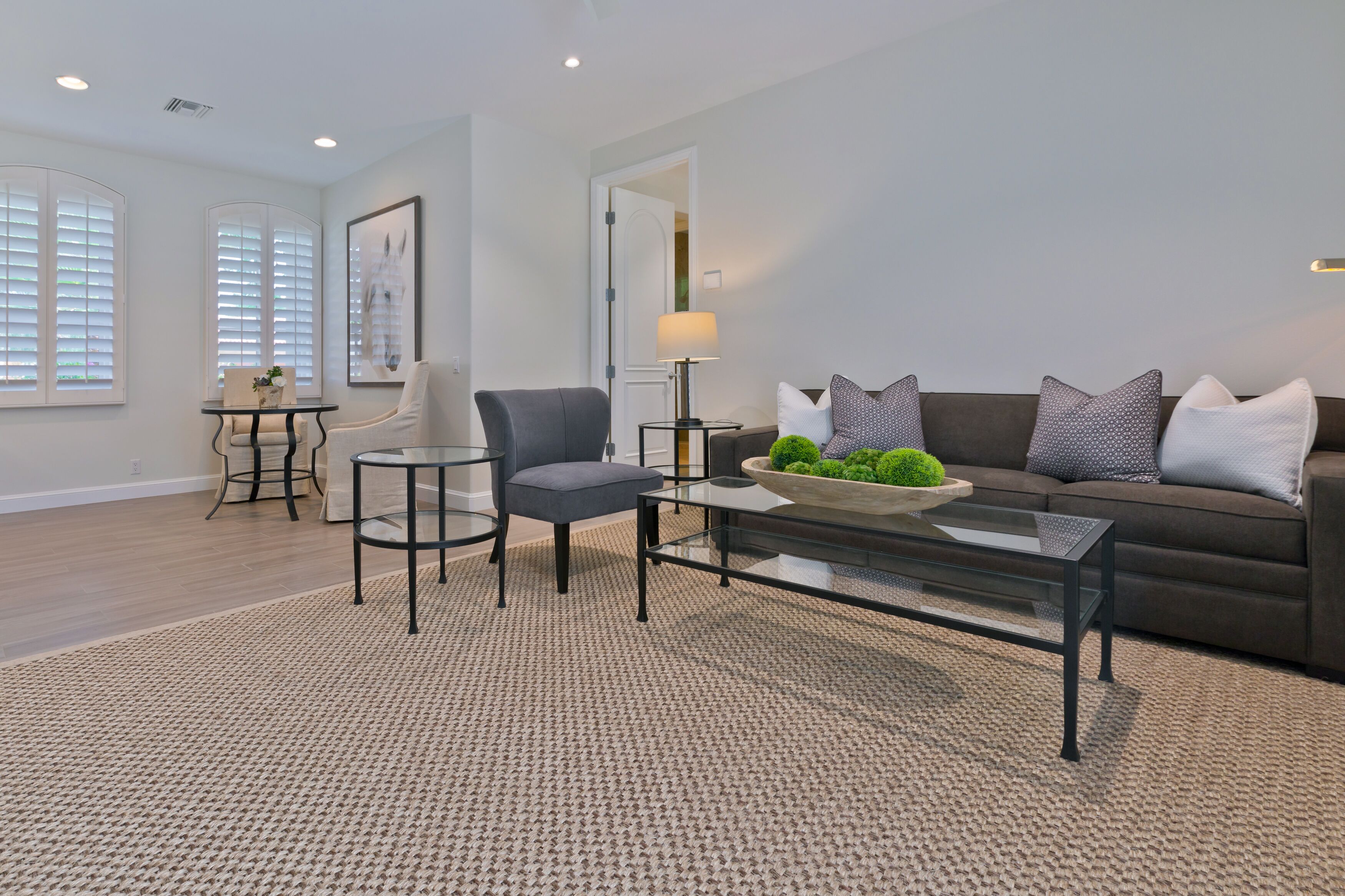A modern living room with a grey sofa, a glass coffee table, and a grey armchair.