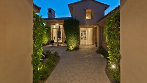 Un sentiero in pietra conduce a una casa con tetto in tegole, circondata da vegetazione e un ingresso ben illuminato.