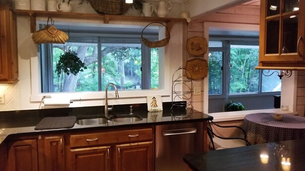 Una cocina con armarios de madera, un lavamanos de acero inoxidable y ventana con vistas a un bosque.