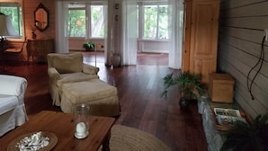 Un salón espacioso con un sofá grande, una mesa de centro y una mesa de comedor. Hay plantas en macetas y un aparador de madera.