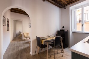 A dining area with a table set for two, a black refrigerator, and a window with a view of the street.