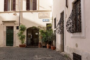 Eine enge Kopfsteinpflasterstraße mit Hauseingang, Blumentöpfen und einem Schild mit der Aufschrift 'VIA R. VIII DEGLI SPAGNOLI'.