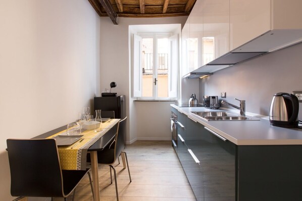 A compact kitchen with a dining area, featuring a window, modern appliances, and a minimalist design.