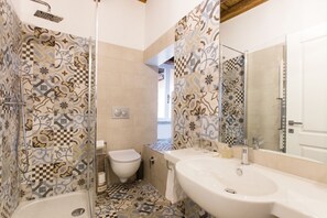 A bathroom with patterned tiles, a shower, a toilet, and a sink with a mirror.