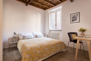 Ein Schlafzimmer mit einem Bett, einem Schreibtisch, einem Stuhl, einem Fenster und einer Heizung.