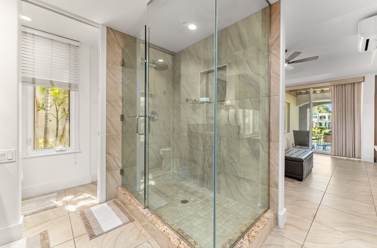 A modern bathroom with a glass-enclosed shower, marble tiles, and a view to the outside.
