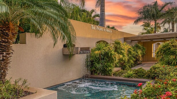 A pool area with a waterfall feature, surrounded by lush greenery and palm trees. - #1301 Ocean Views, 1st Floor, Best location, Courtyard, Great Promotion (Kihei)