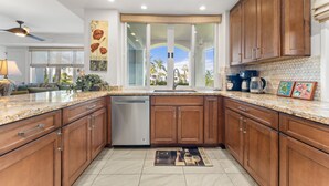 A modern kitchen with wooden cabinets, granite countertops, and a dishwasher. - #1301 Ocean Views, 1st Floor, Best location, Courtyard, Great Promotion (Kihei)