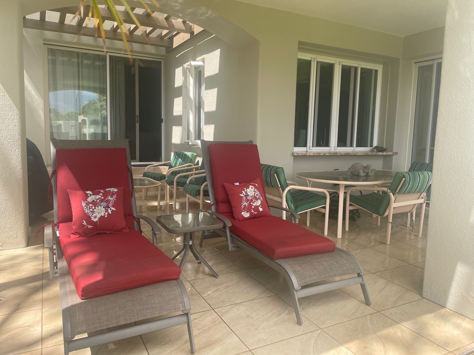 Une terrasse ensoleillée avec deux chaises longues rouges, une petite table et un coin repas avec des chaises.