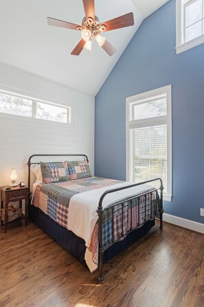 Relax in a cozy room with a four-poster bed, ceiling fan, and window with blinds.