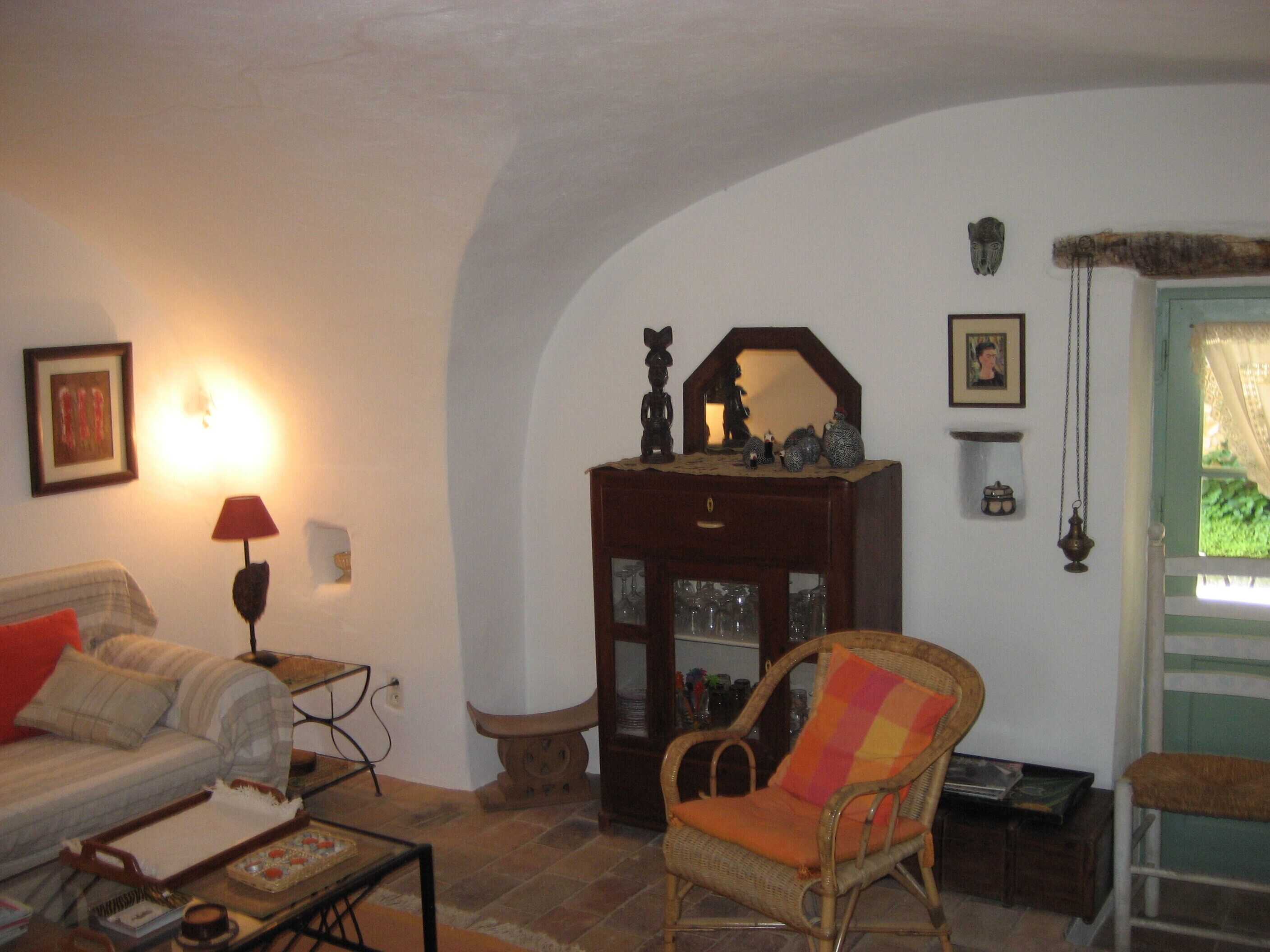 A cozy living room with a wicker chair, a sofa, a wooden cabinet, and a framed picture on the wall.