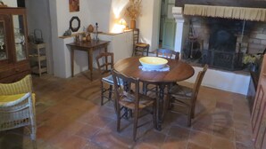 A cozy dining area with a round wooden table, chairs, and a fireplace. - COTTAGE WITH HEATED POOL - MAS IN THE GARRIGUE D'UZES (Fons-Sur-Lussan)